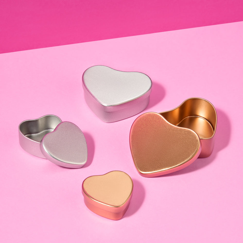Sammlung von Herzblechdosen in Silber und Roségold auf rosa Hintergrund